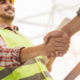 Side view of a smiling man in protective reflective vest shaking hands with an person that is out of frame